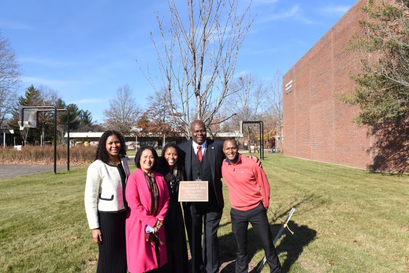 Pamerson Ifill '89 stands with three family members at a tree planted in his honor at Massasoit Community College near the Field House.